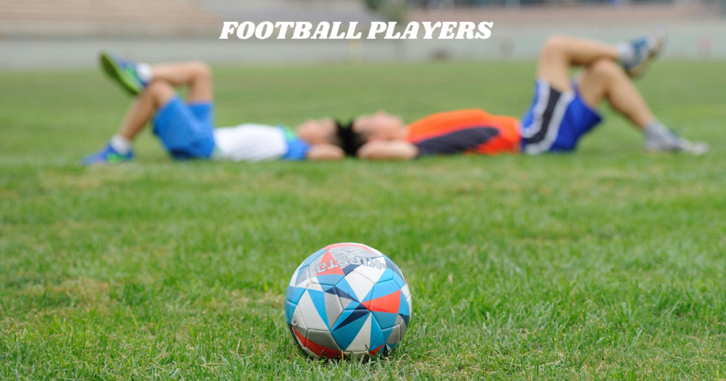 Blured image of Two football players from different teams lying down on a grassy ground with a clear image of football,