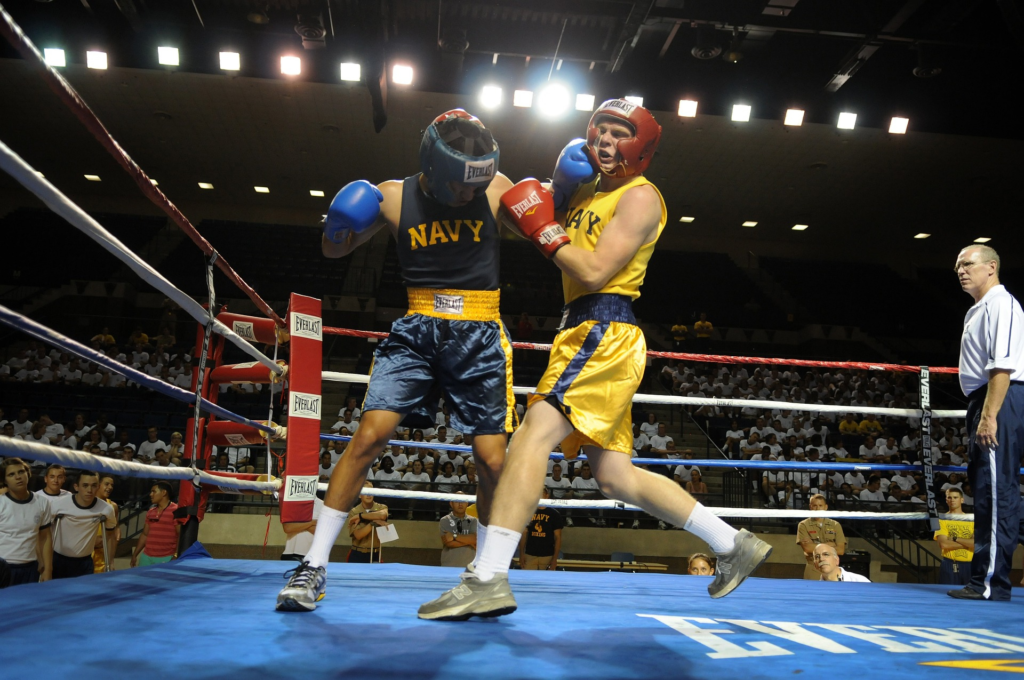 Boxing: Two boxers exchanging punches in a boxing ring, referee watching in surprise, surrounded by cheering crowd.