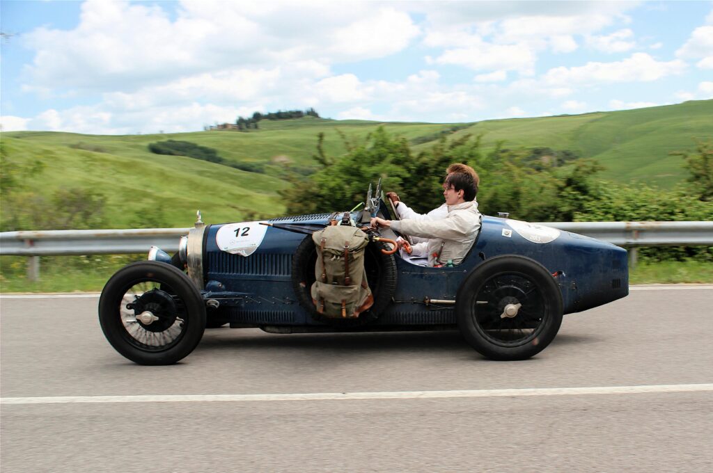 Sports Cars enthusiasts admire a classic Bugatti Type 35 driven by men on a scenic Tuscan road.